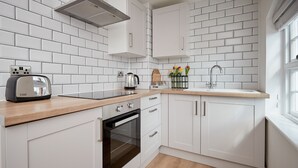 A modern kitchen with white cabinetry, a wooden countertop, a built-in oven, and a window providing natural light. - Lovely Quiet Cottage in Kemerton! (Tewkesbury)