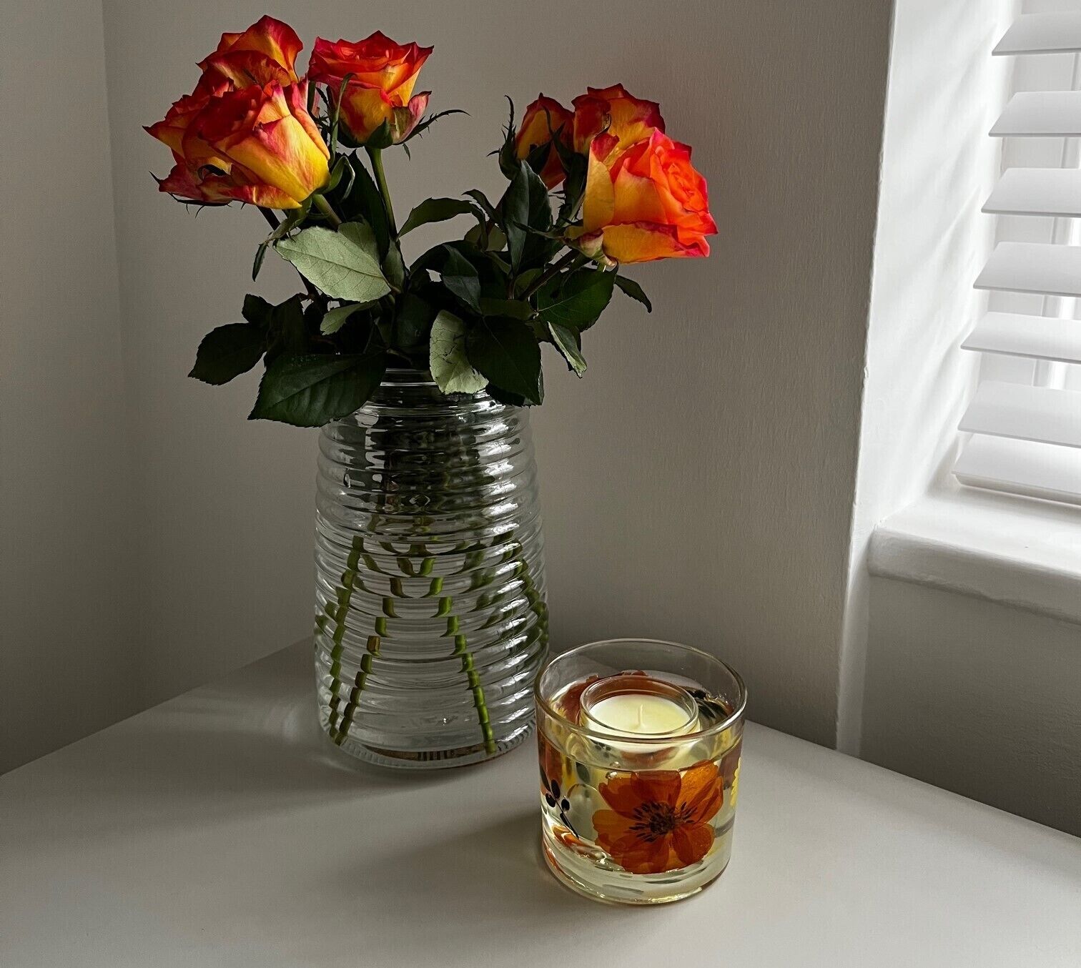 A clear glass vase with roses and a candle on a table.
