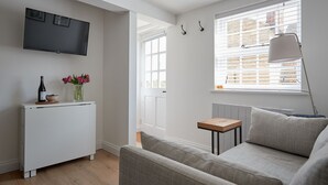A modern living room with a white radiator, a grey sofa, a small wooden table, and a floor lamp. - Lovely Quiet Cottage in Kemerton! (Tewkesbury)