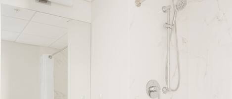 A modern bathroom with a marble wall, a wooden vanity, and a shower with a handheld showerhead.
