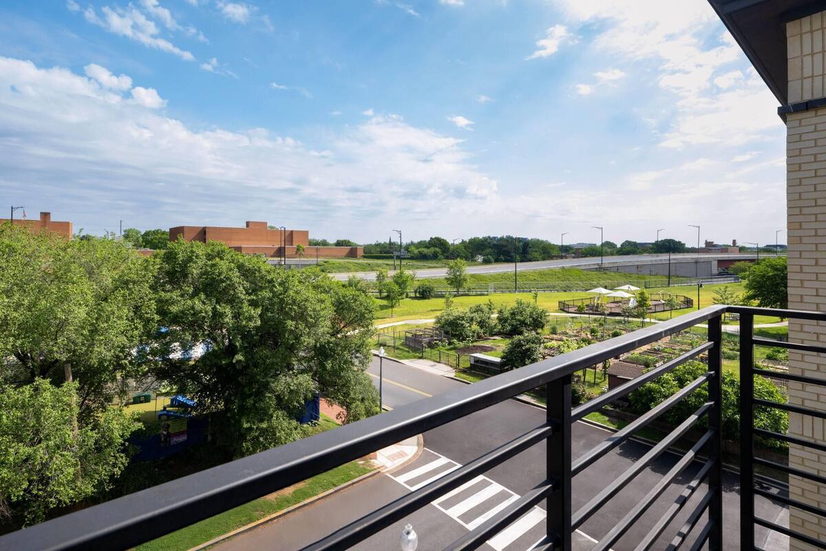 A view from a balcony overlooking a parking lot, a green park area, and distant buildings.
