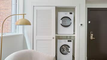 A laundry room with two white washing machines, a beige chair, and a floor lamp.