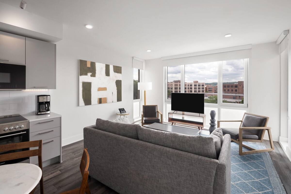 A modern living room with a gray sofa, a flat-screen TV, and a dining area with a table and chairs.