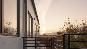 Un balcón con una banca y una mesita, con vistas a un edificio y al atardecer.