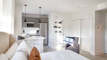 A modern hotel room with a bed, a chair, a desk, and a kitchenette.