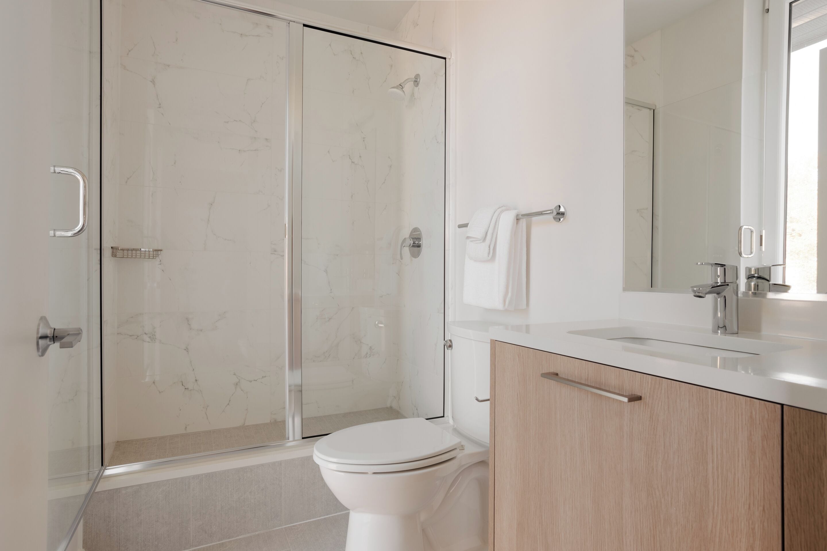 Ein modernes Badezimmer mit einer Duschkabine aus Glas, einer weißen Toilette und Holzschränken.