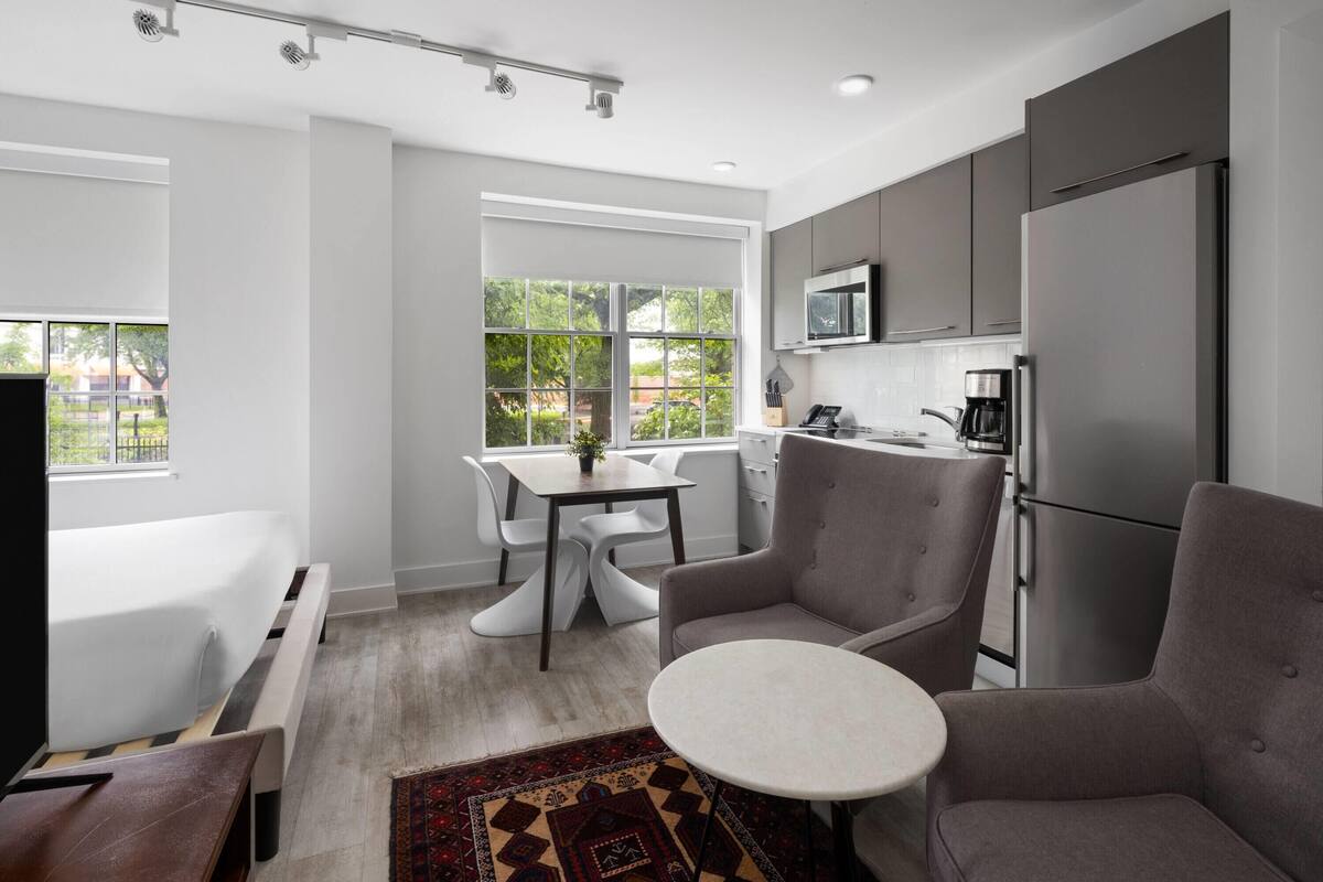 A modern kitchen with grey cabinets, a stainless steel refrigerator, and a dining area with a table and chairs.