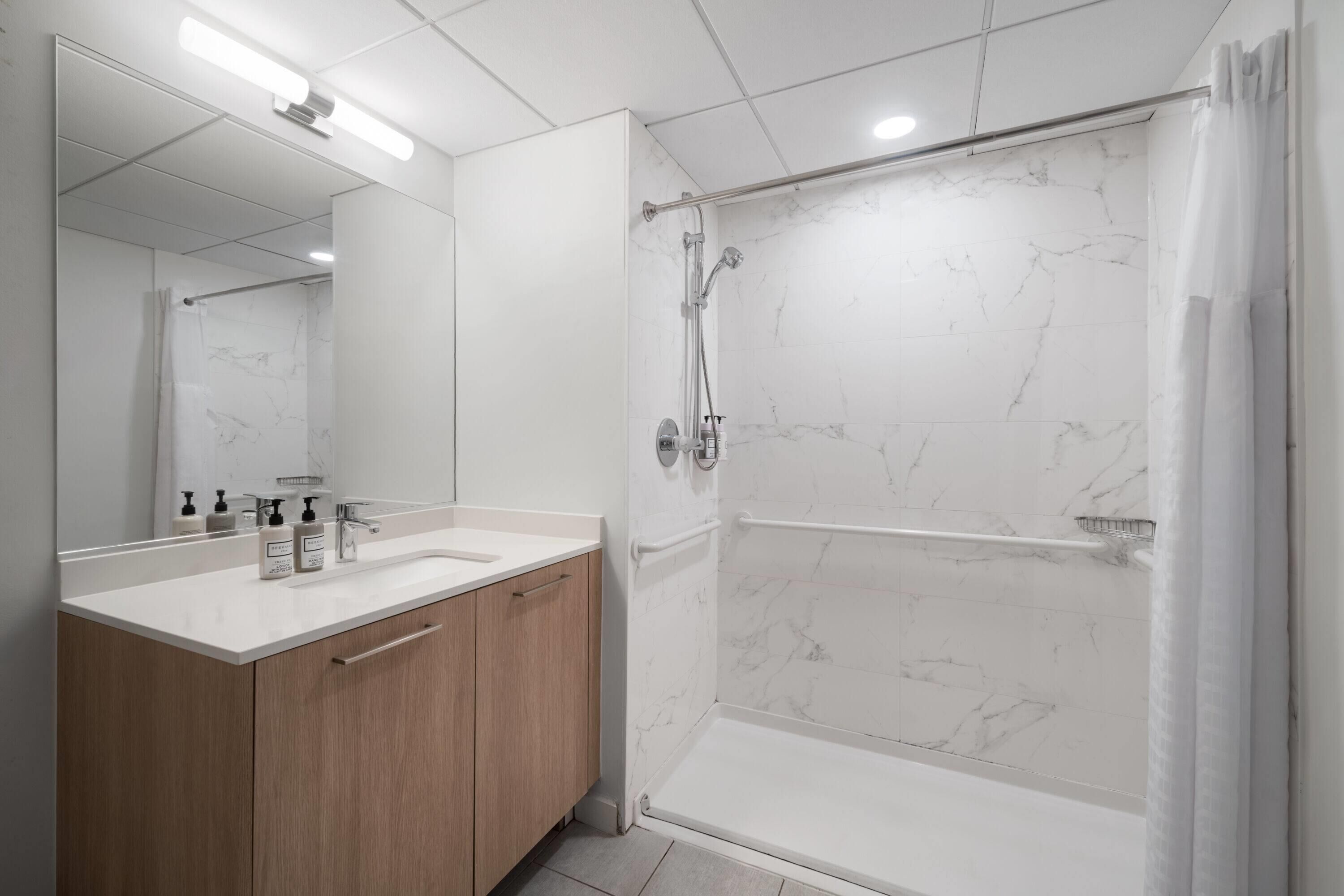 Un baño moderno con ducha de mármol, tocador de madera y un espejo grande.