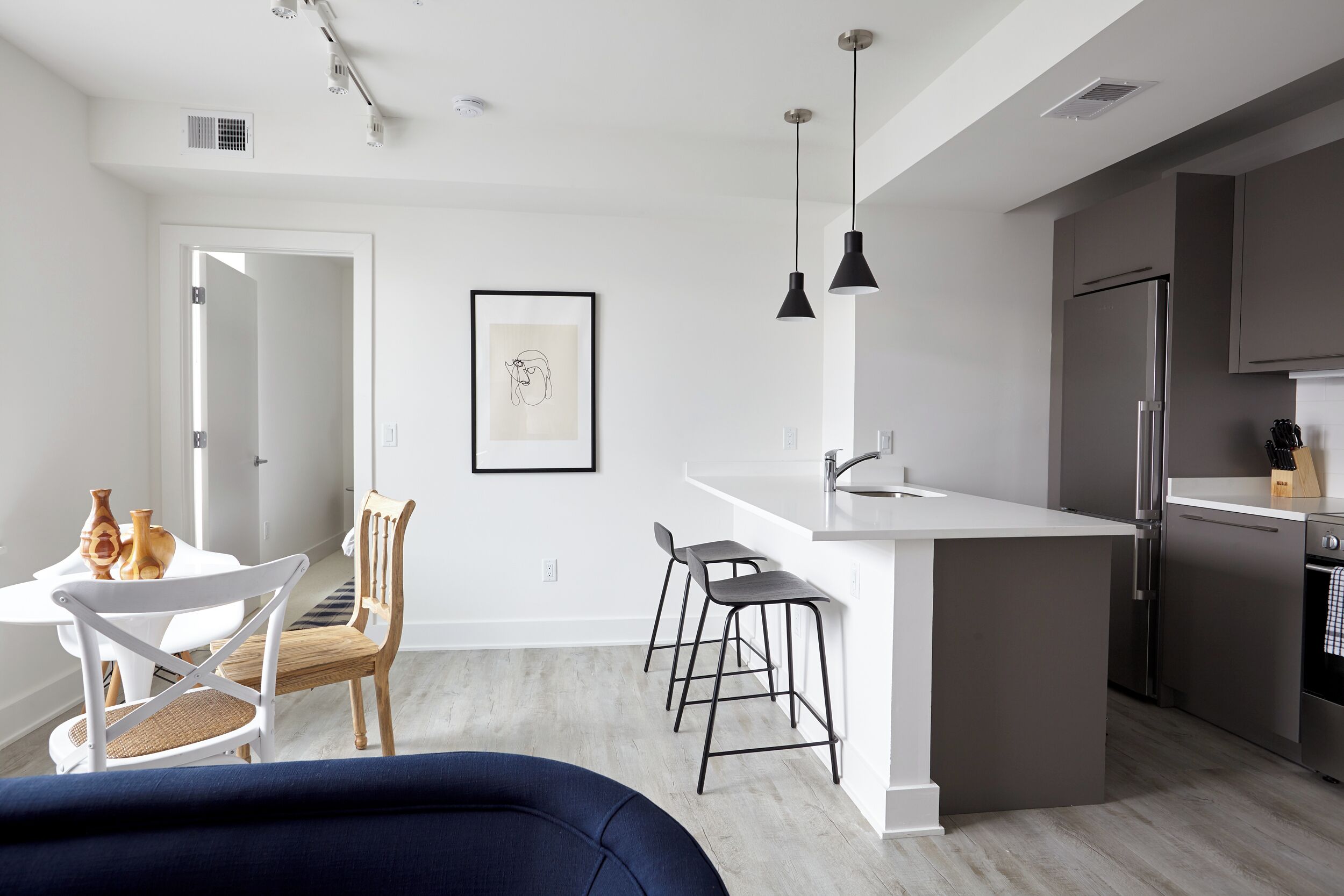 A modern kitchen with a white island, black bar stools, and a stainless steel refrigerator.