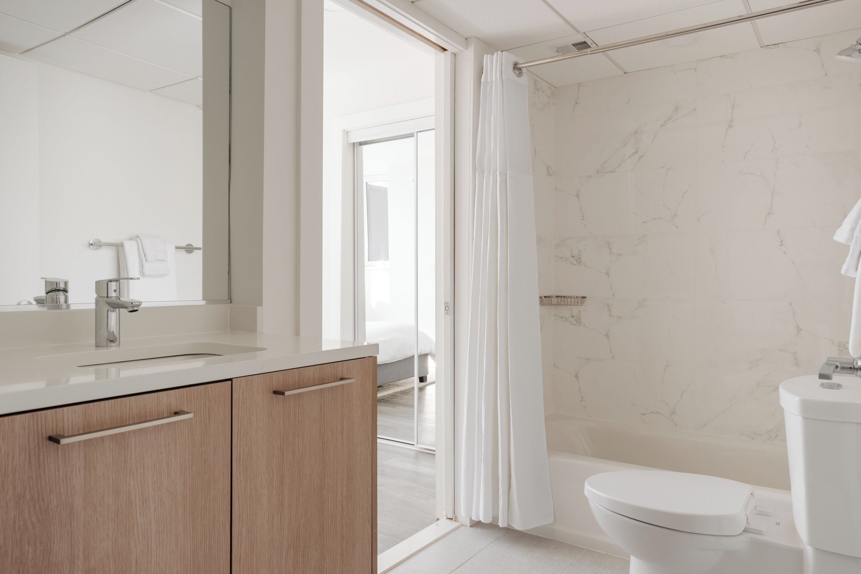 A modern bathroom with a marble wall, a white sink, and a toilet.