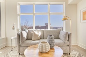 A living room with a sofa, two vases, a lamp, and a view through large windows. - Reside Navy Yard, a Wyndham Residence (Washington)