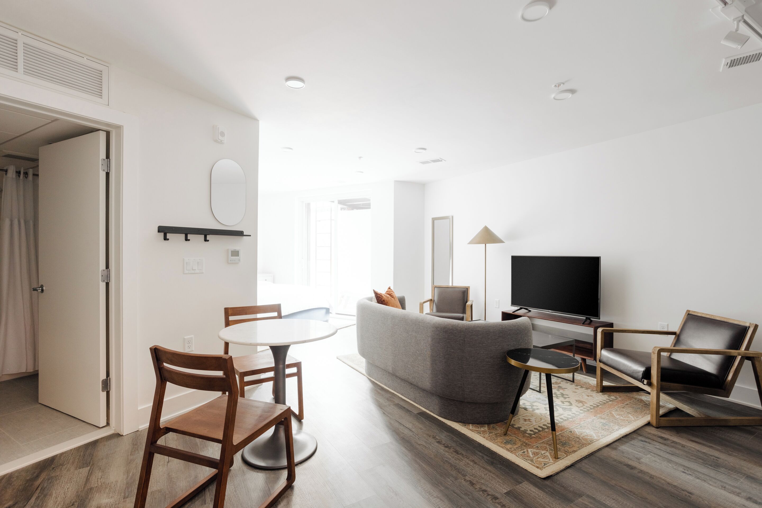 A modern living room with a grey sofa, wooden chairs, a TV, and a flat-screen TV on a stand.