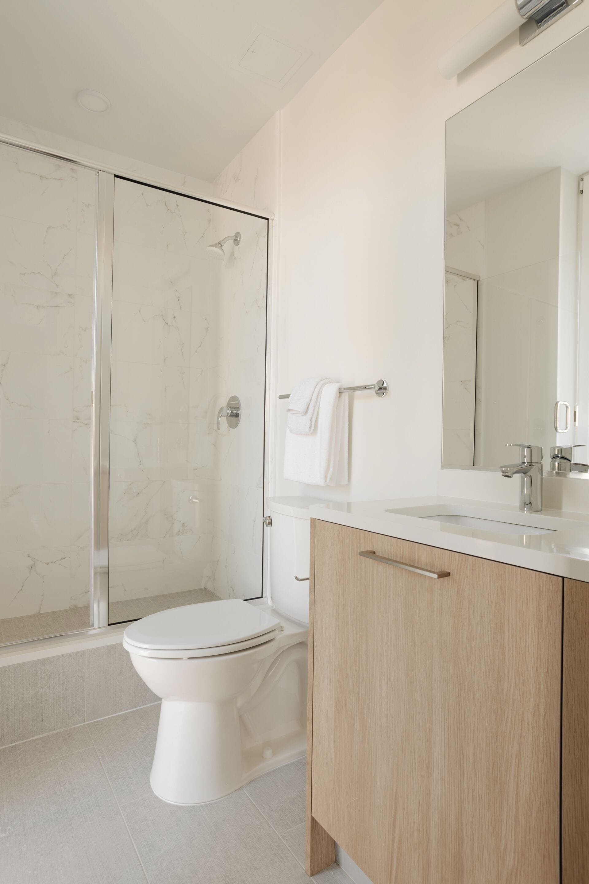 Un baño moderno con cabina de ducha de vidrio, inodoro blanco y tocador de madera con espejo.