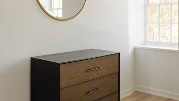 A room with a wooden dresser, a round mirror, and a window.
