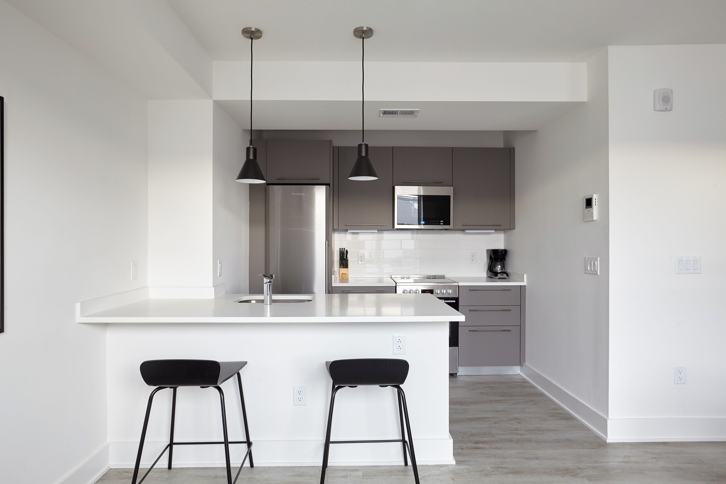 A modern kitchen with a white island, stainless steel appliances, and black bar stools.
