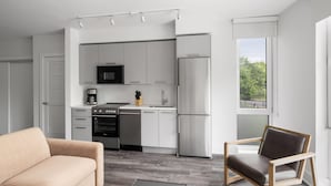 Una cocina moderna con armarios blancos, un microondas y un refrigerador. Hay un sofá color beige y una silla de madera con cojín.