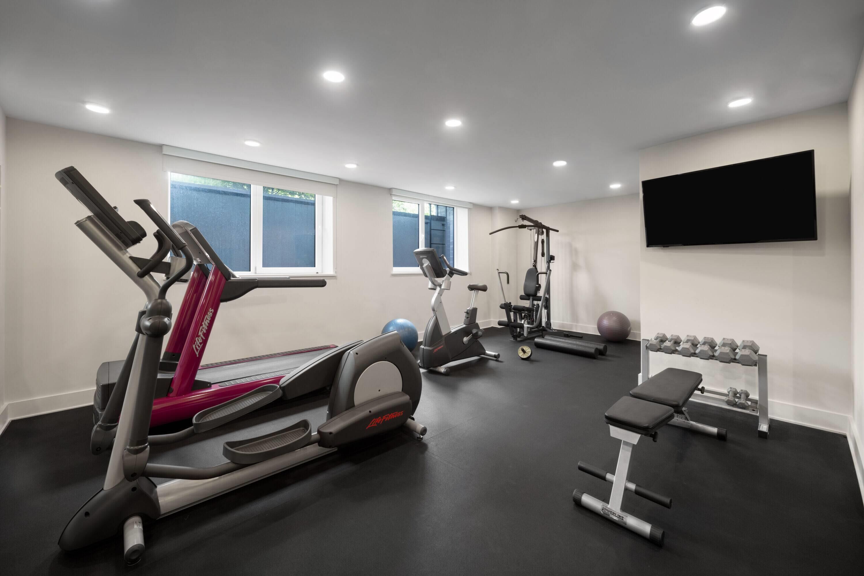 A gym with treadmills, an elliptical, a bench, and dumbbells.