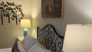 Un lit bien fait, avec du linge de lit blanc et un coussin à motifs noir et blanc. Une lampe avec un pied bleu et un abat-jour blanc est posée sur la table de chevet. Une télécommande se trouve également sur la table.