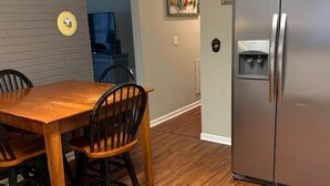 Un coin repas avec une table et des chaises en bois, un réfrigérateur en acier inoxydable et un mur bleu.