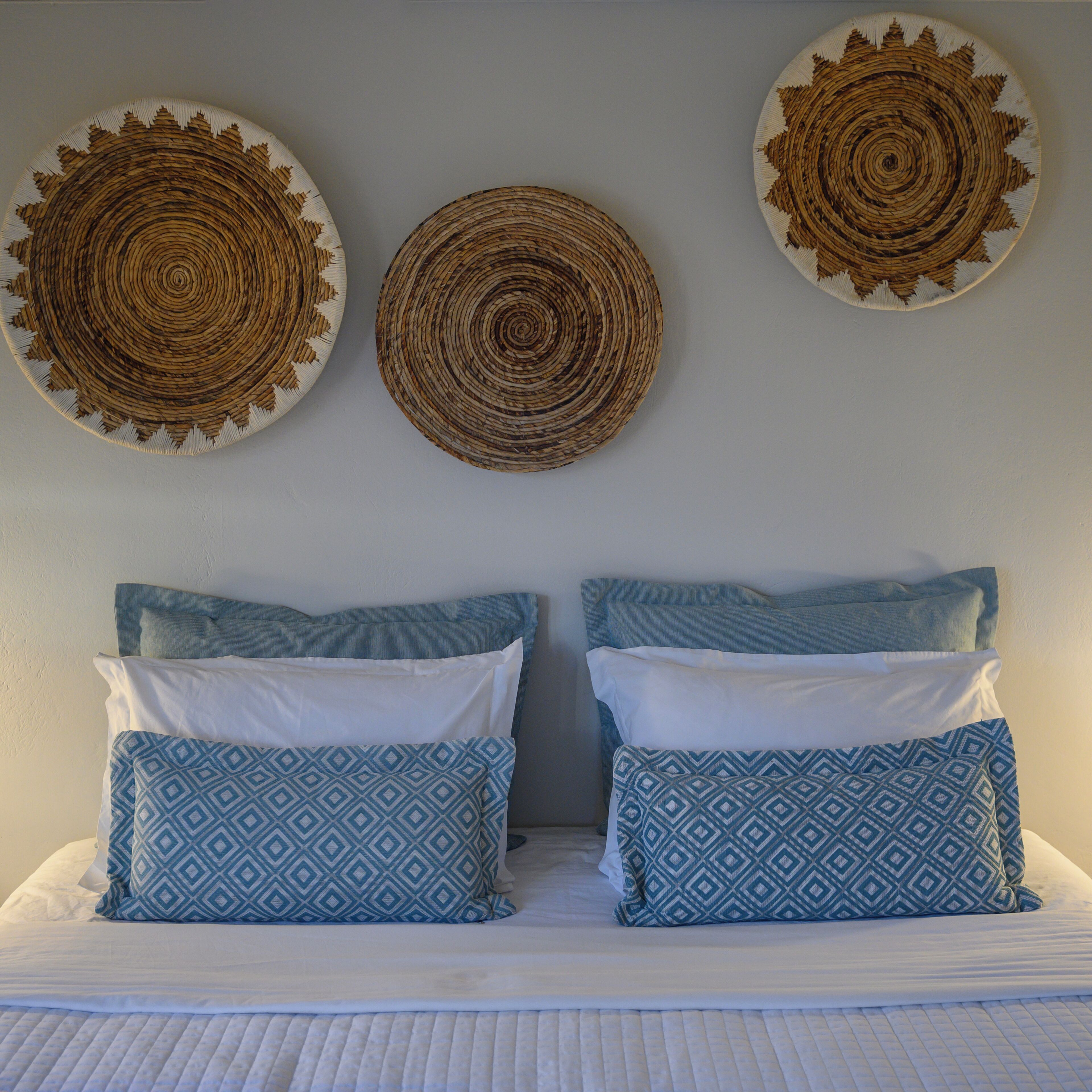 A bed with two pillows and two wall-mounted circular woven wall hangings.