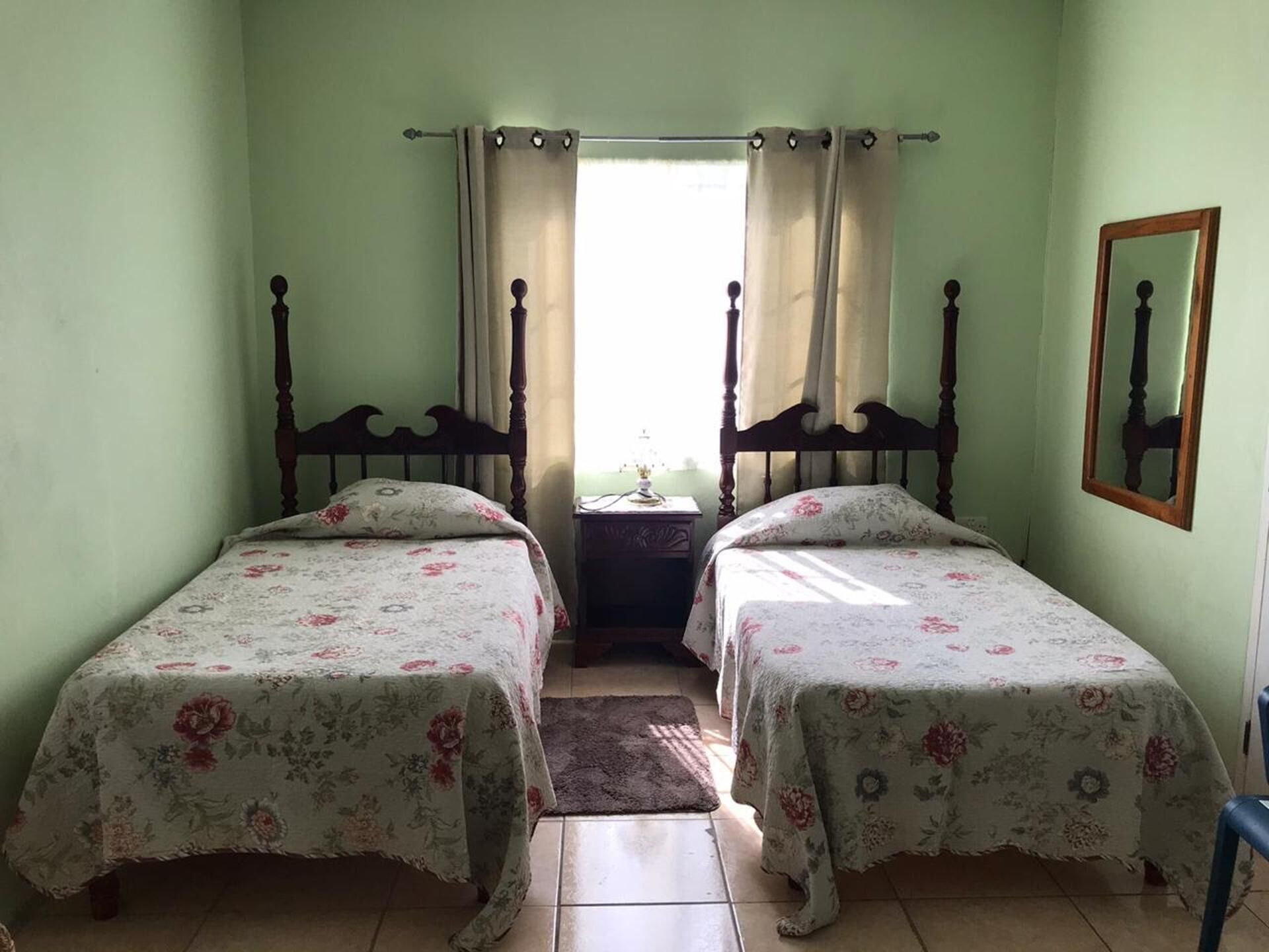 A bedroom with two single beds, a nightstand, a mirror, and a window with curtains.