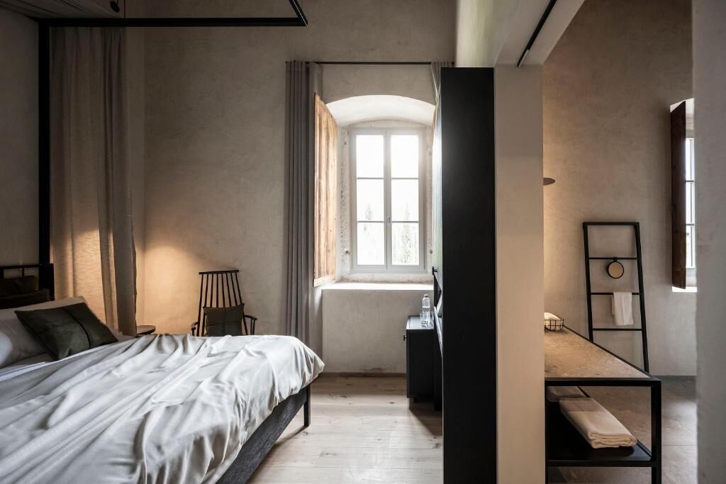 A bedroom with a bed, a desk, a chair, a window, and a radiator.