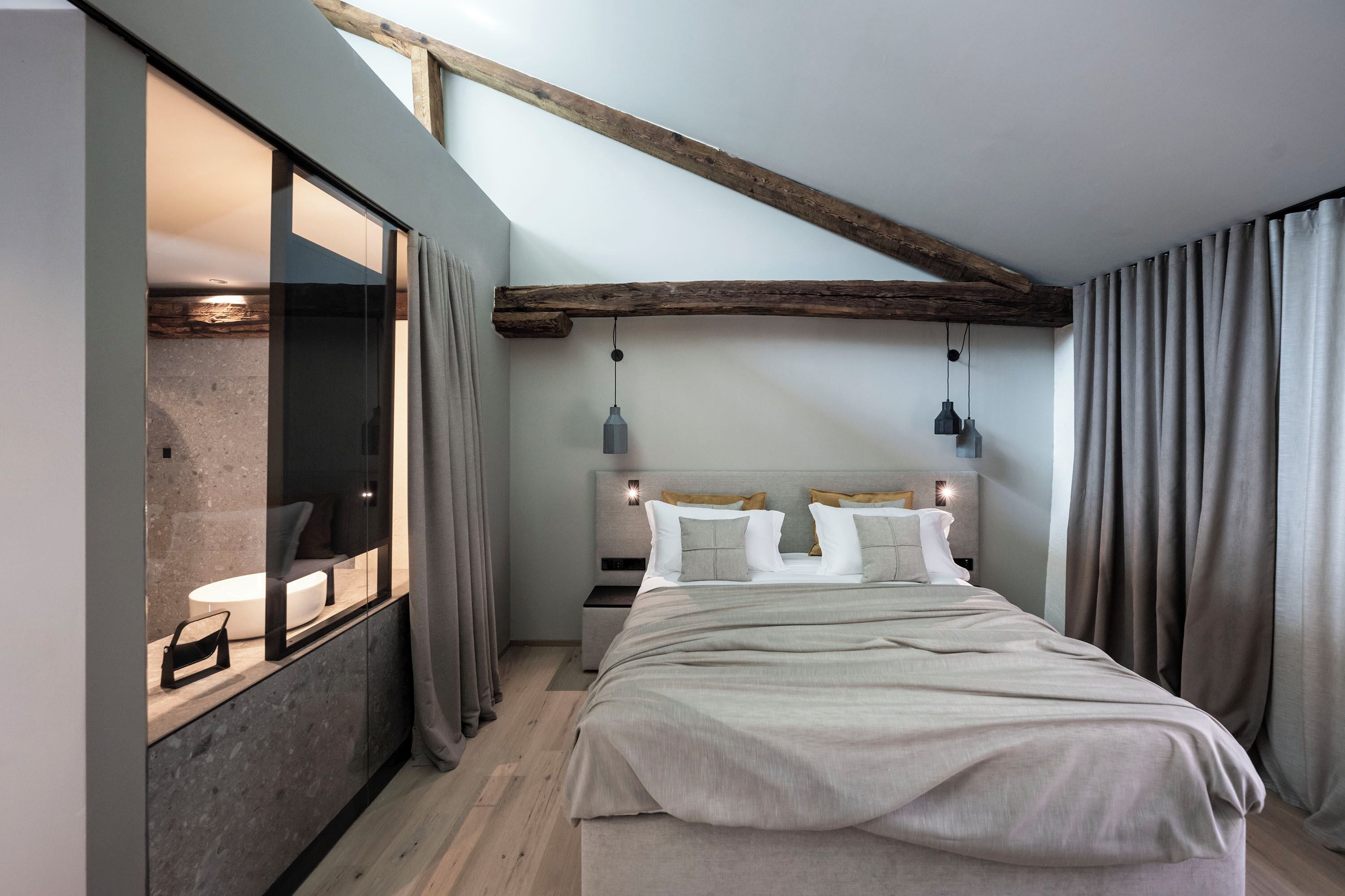 Een moderne slaapkamer met een groot bed, een inbouwkbank en een raam met gordijnen.