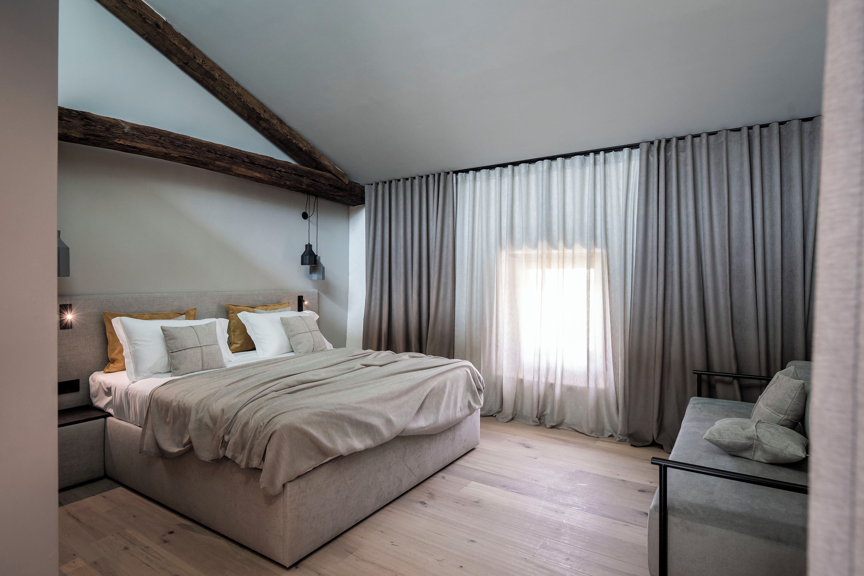 A bedroom with a large bed, wooden beams, a nightstand, and a sofa.
