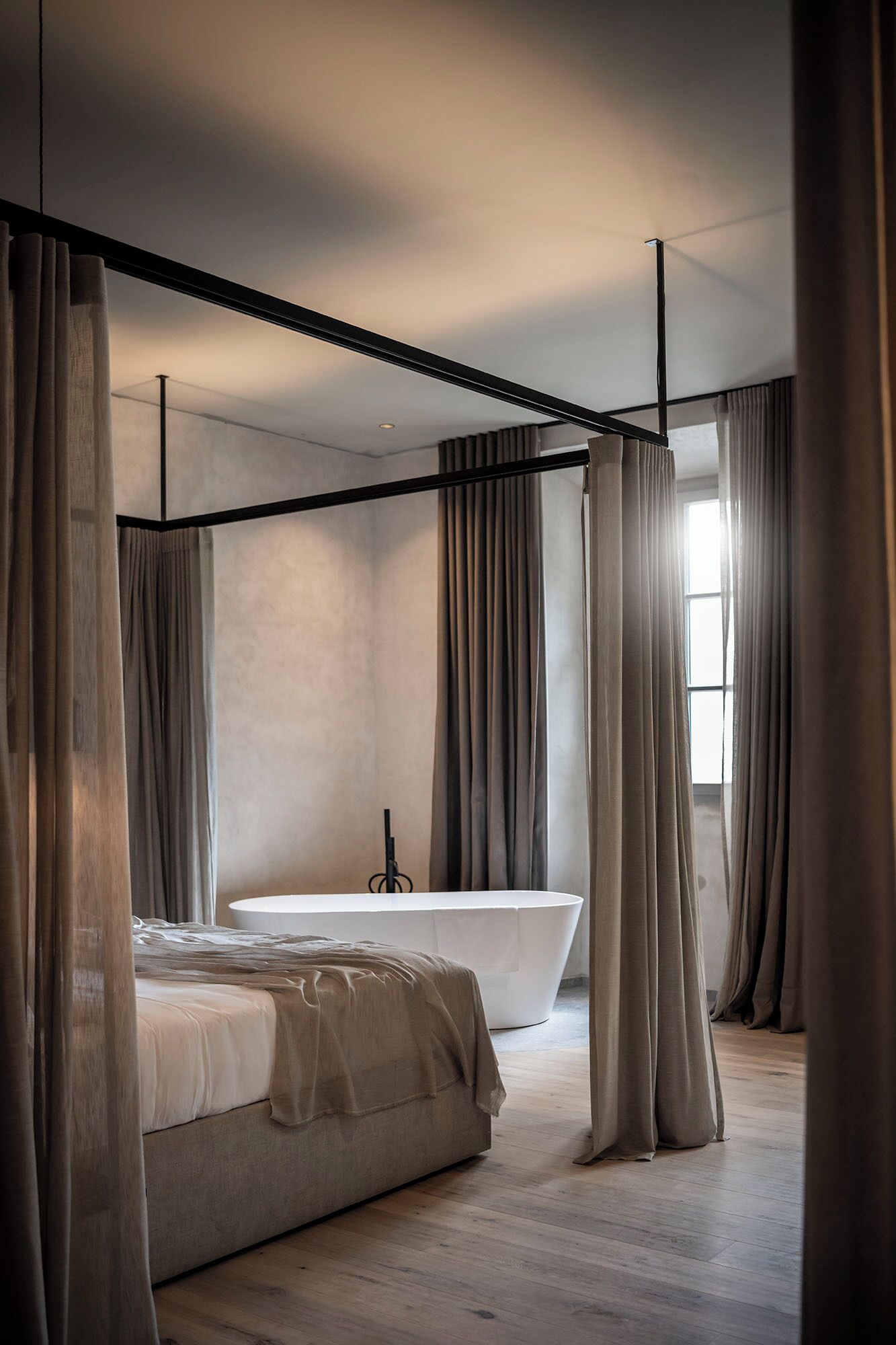 Un dormitorio moderno con una cama grande, una bañera independiente y cortinas gruesas.