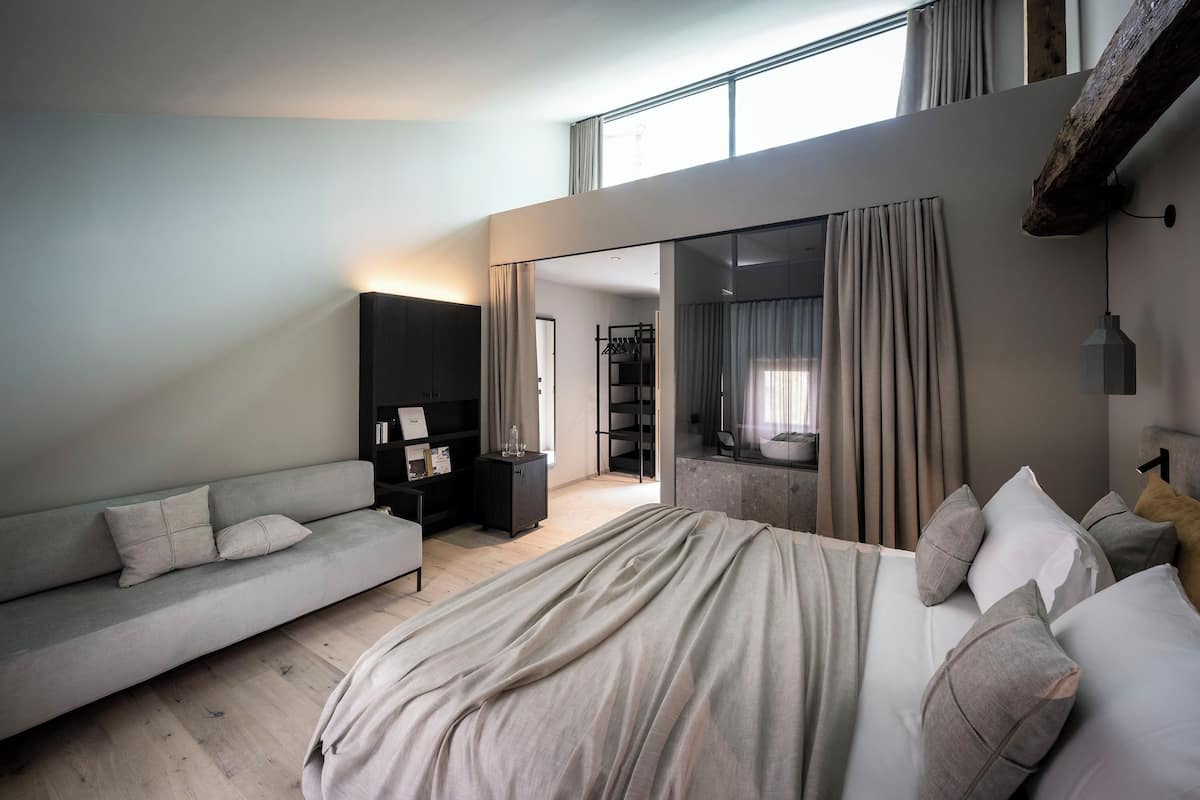 A modern bedroom with a large bed, a sofa, a wardrobe, and a walk-in closet.