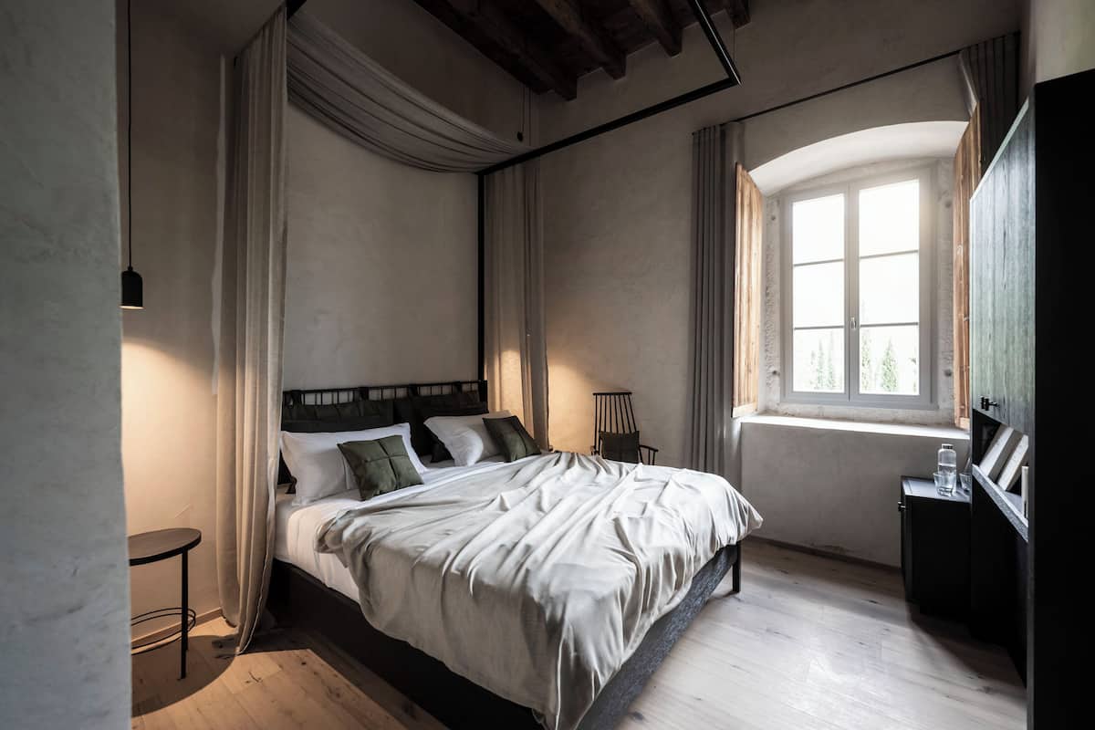 A bedroom with a large bed, a window with curtains, a bedside table, and a small table by the window.