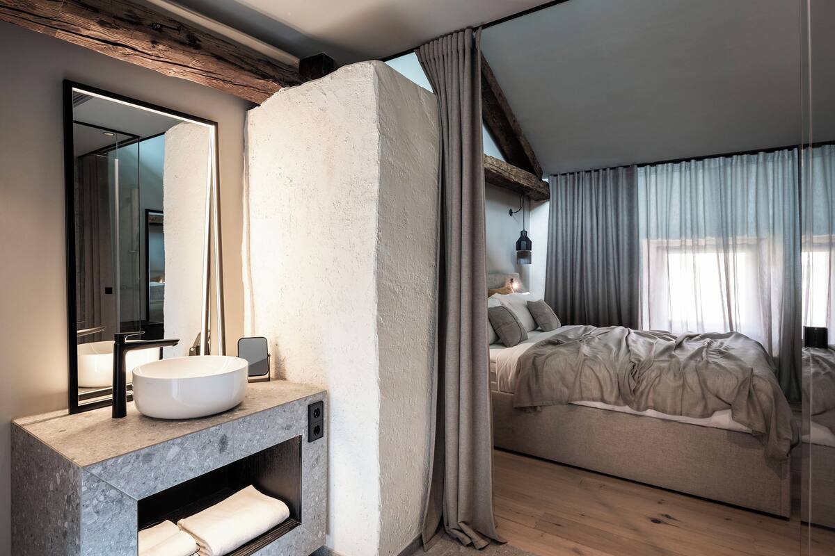 A modern bedroom with a large bed, a built-in vanity with a sink, and a large mirror.