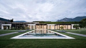 A modern building with a central reflective pool, surrounded by well-maintained lawns and a mountainous backdrop. - Monastero ARX VIVENDI (Arco)