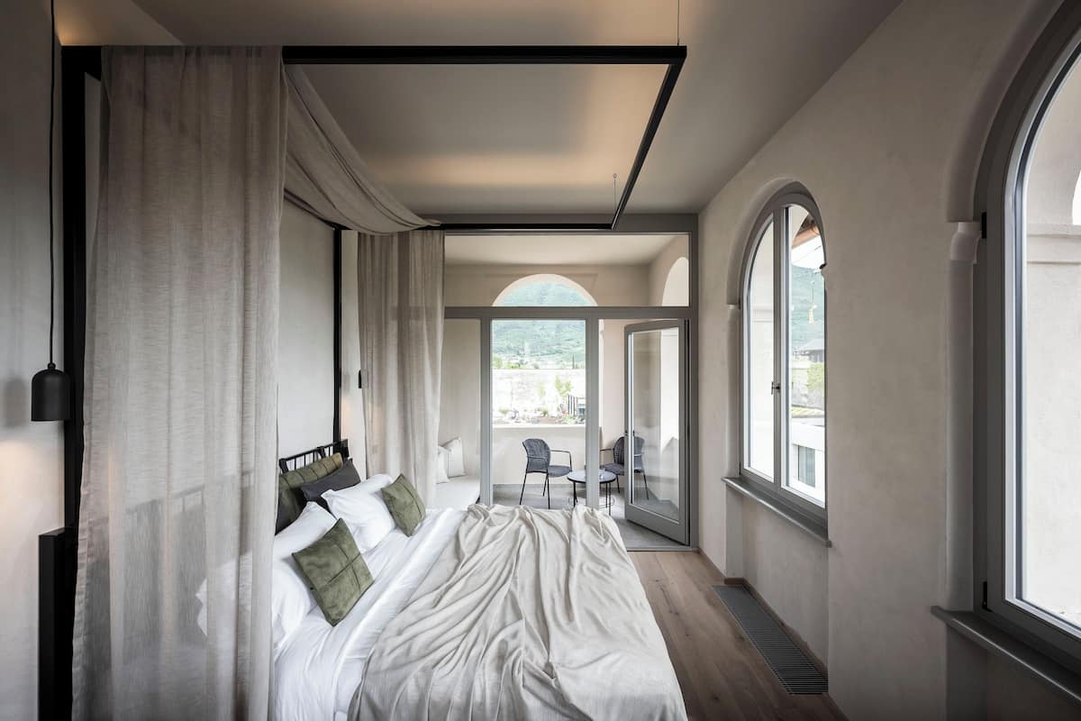 A modern hotel room with a large bed, a balcony with a chair, and large windows.