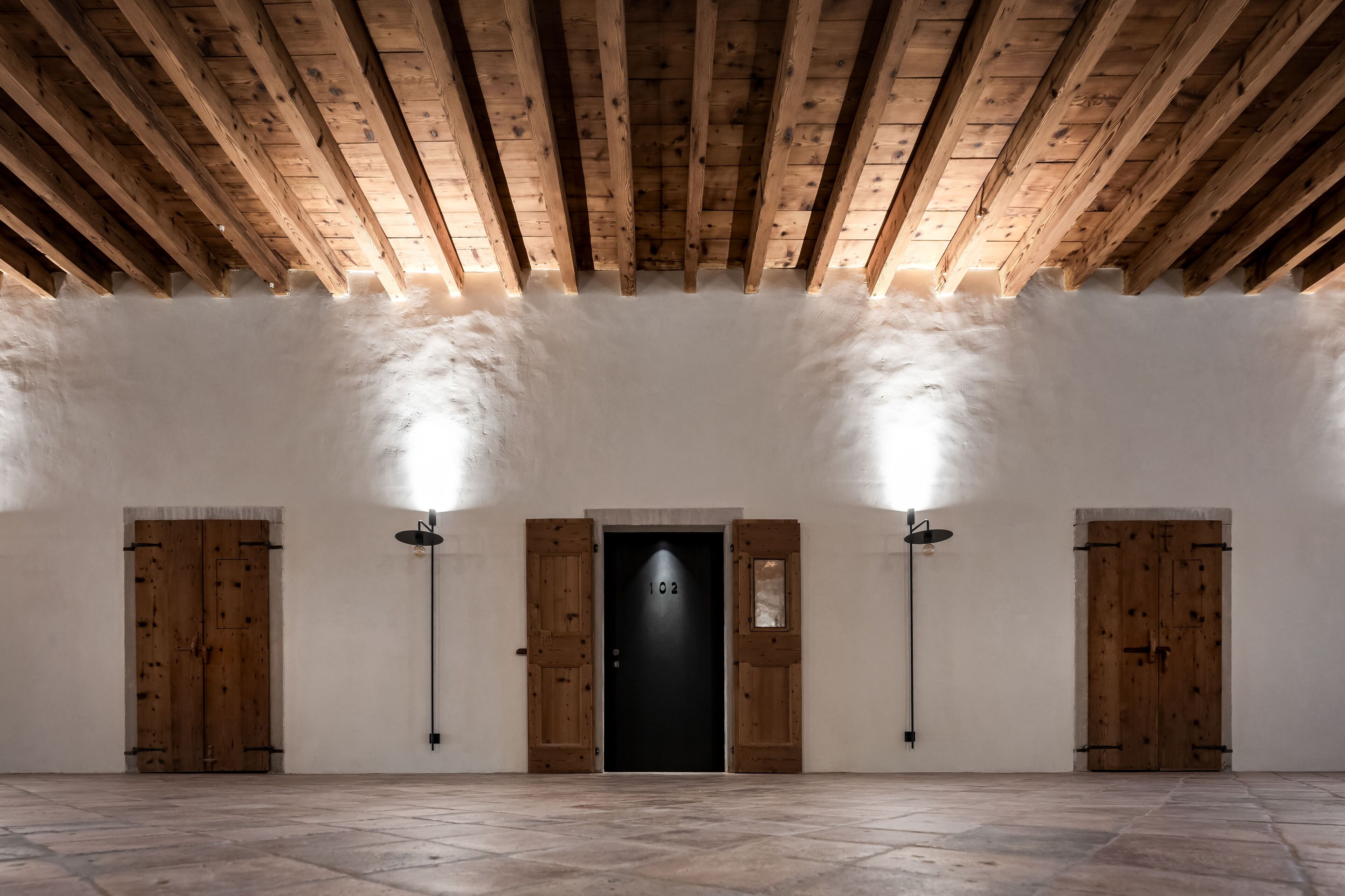 Une pièce spacieuse avec un haut plafond en bois, une porte noire portant le numéro 102, et deux portes en bois de chaque côté.