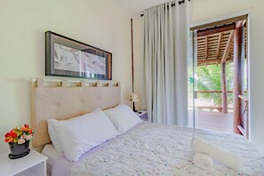 A hotel room with a bed, a nightstand, a lamp, a framed picture, and a view of the outdoors. - IT26 Bangalô 3 Suítes - Itacimirim (Camaçari)