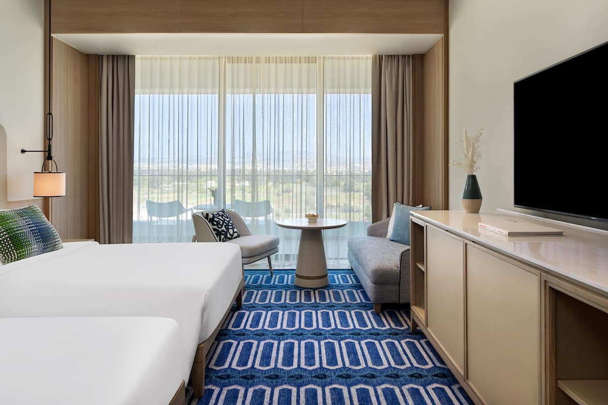 Ein Hotelzimmer mit Bett, Schreibtisch, Stuhl, Fernseher und einem großen Fenster mit Vorhängen.