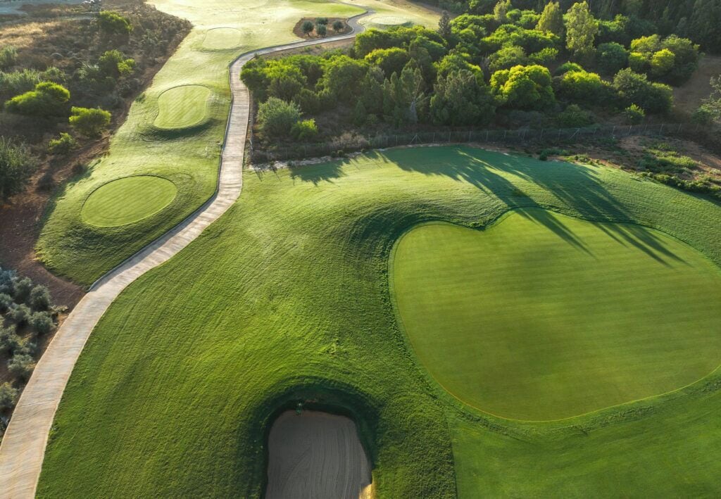 A golf course with a winding path, sand bunkers, and dense trees.