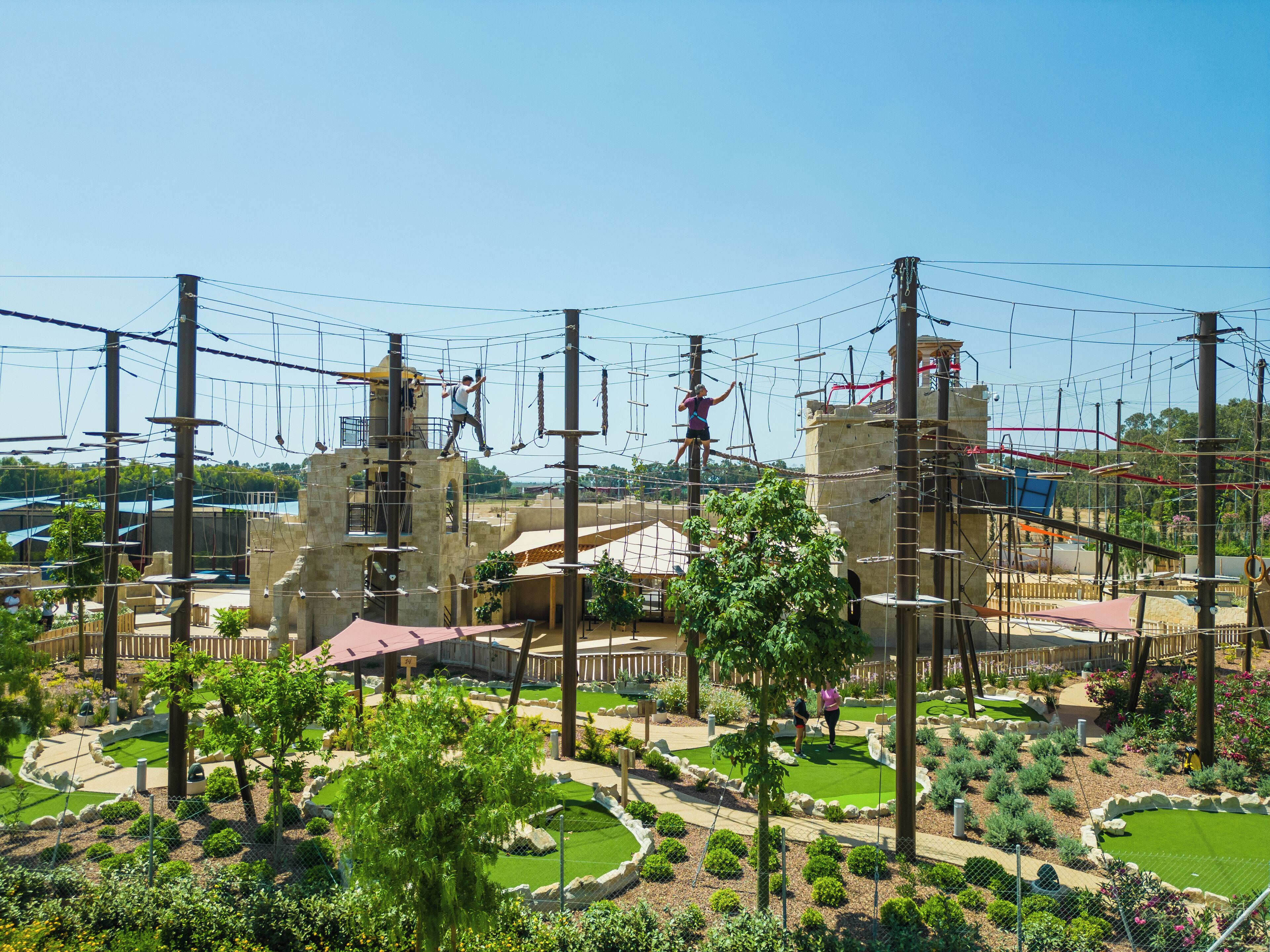 An outdoor adventure park with rope bridges, climbing structures, and landscaped gardens.