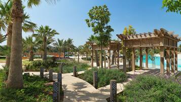Stroll along the winding pathway to a serene pool area surrounded by lush greenery and decorative pillars.