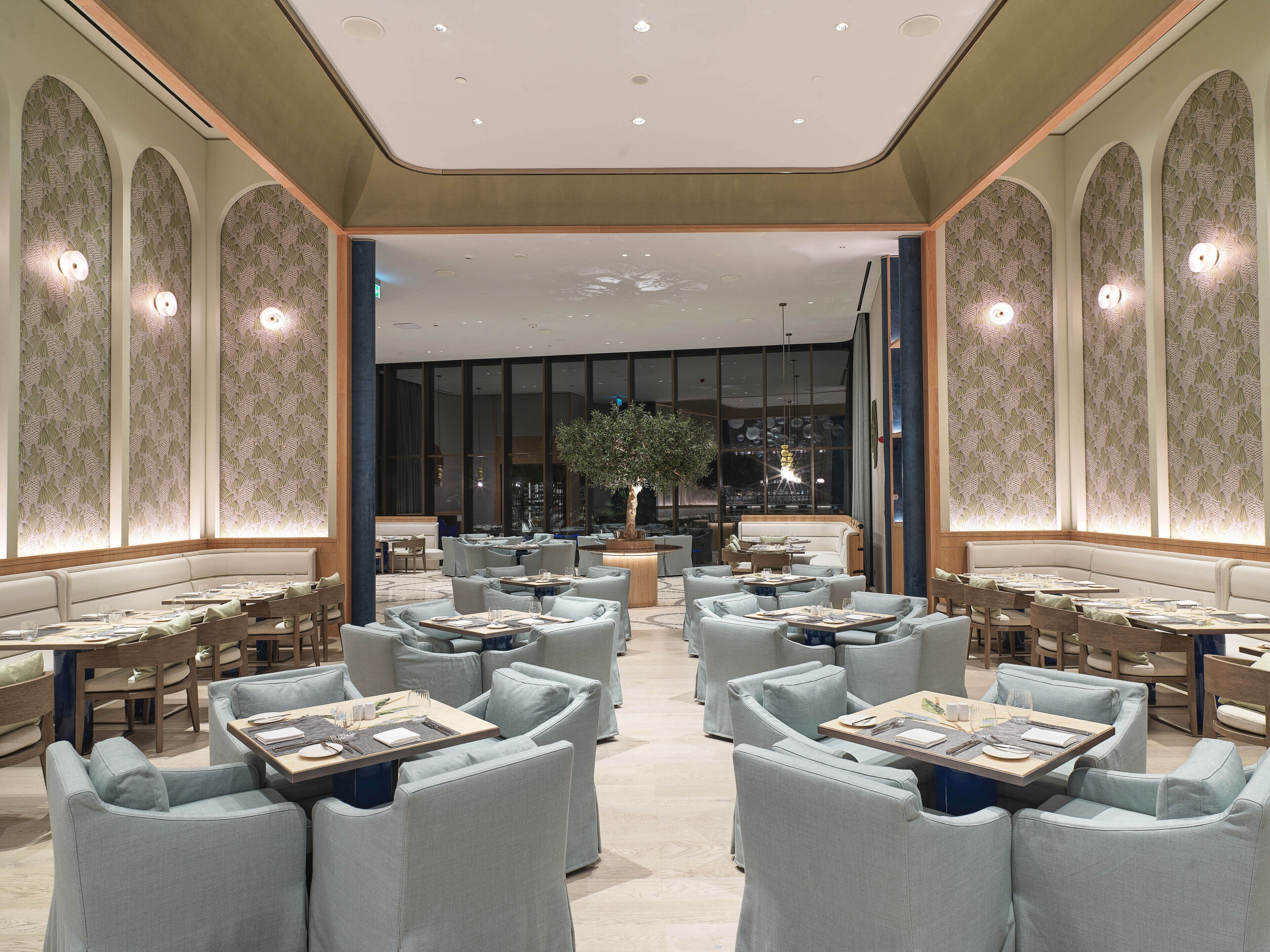 Ein geräumiges, elegant gestaltetes Restaurant mit hohen Decken, gemusterten Wänden und einer zentralen Sitzgruppe mit Tischen und Stühlen.