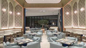 A spacious, elegantly designed restaurant with high ceilings, patterned walls, and a central seating area with tables and chairs.