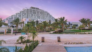 A modern hotel with a large pool area, palm trees, and a well-maintained garden. - City of Dreams Mediterranean - Integrated Resort, Casino & Entertainment (Limassol)