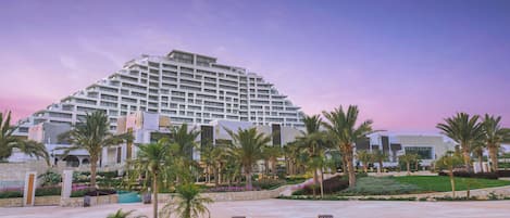 Un hotel moderno con un amplio área de piscina, palmeras y un jardín bien cuidado.