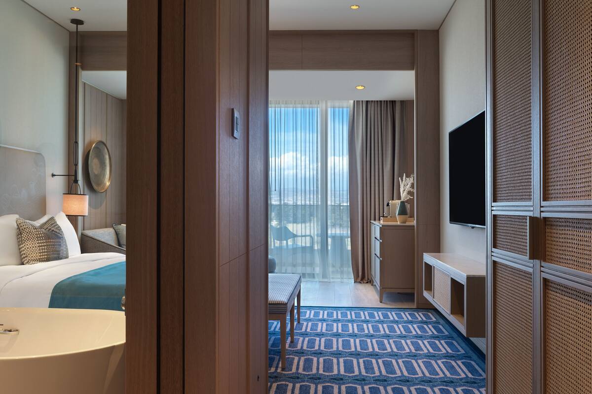 Ein Hotelzimmer mit Bett, Nachttisch, Lampe und Blick auf einen Balkon.