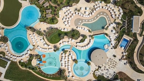 An aerial view of a resort with multiple swimming pools, sun loungers, and palm trees. - City of Dreams Mediterranean - Integrated Resort, Casino & Entertainment (Limassol)