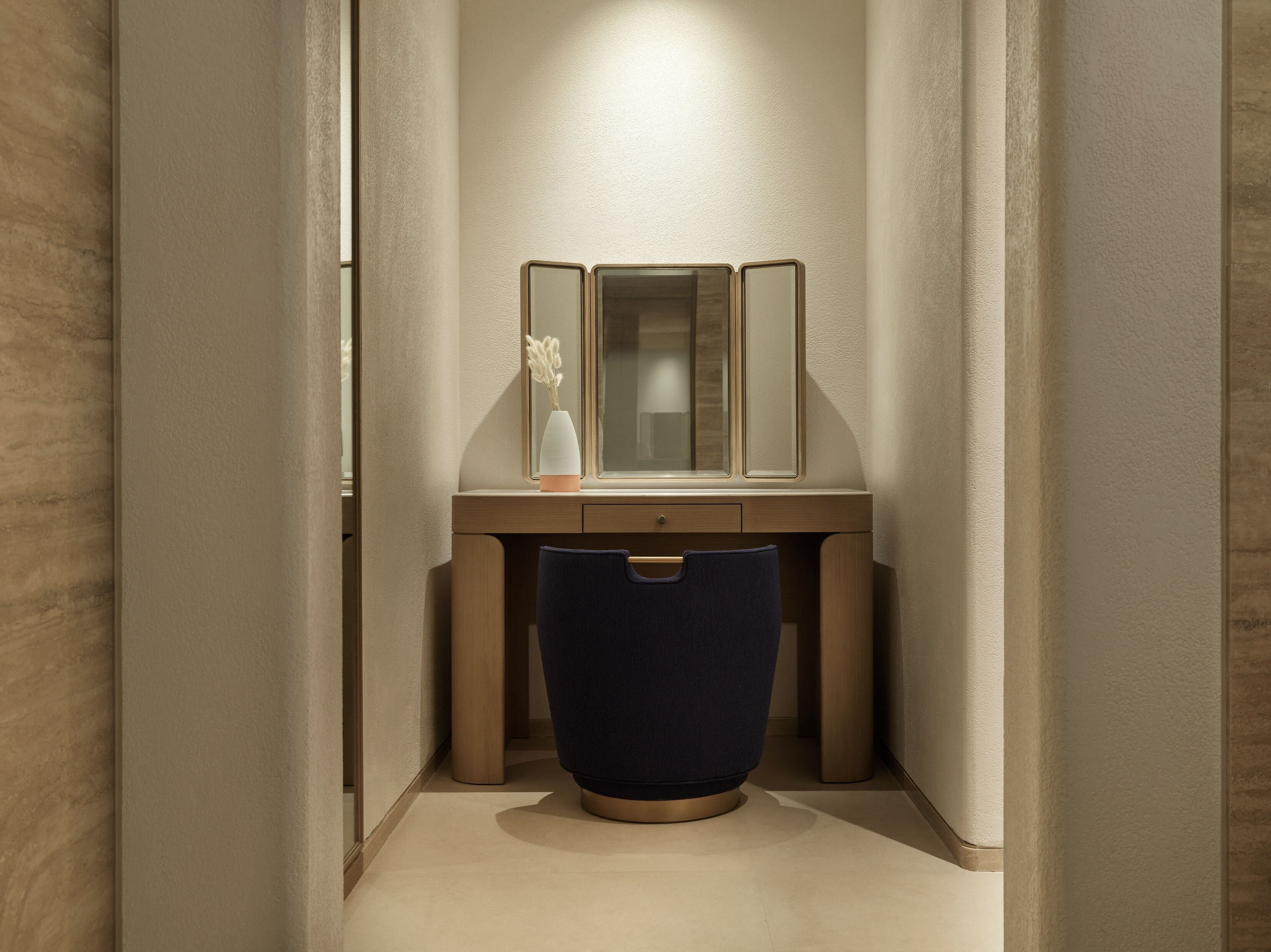 A narrow hallway with a wooden vanity, a mirror, and a vase with dried flowers.