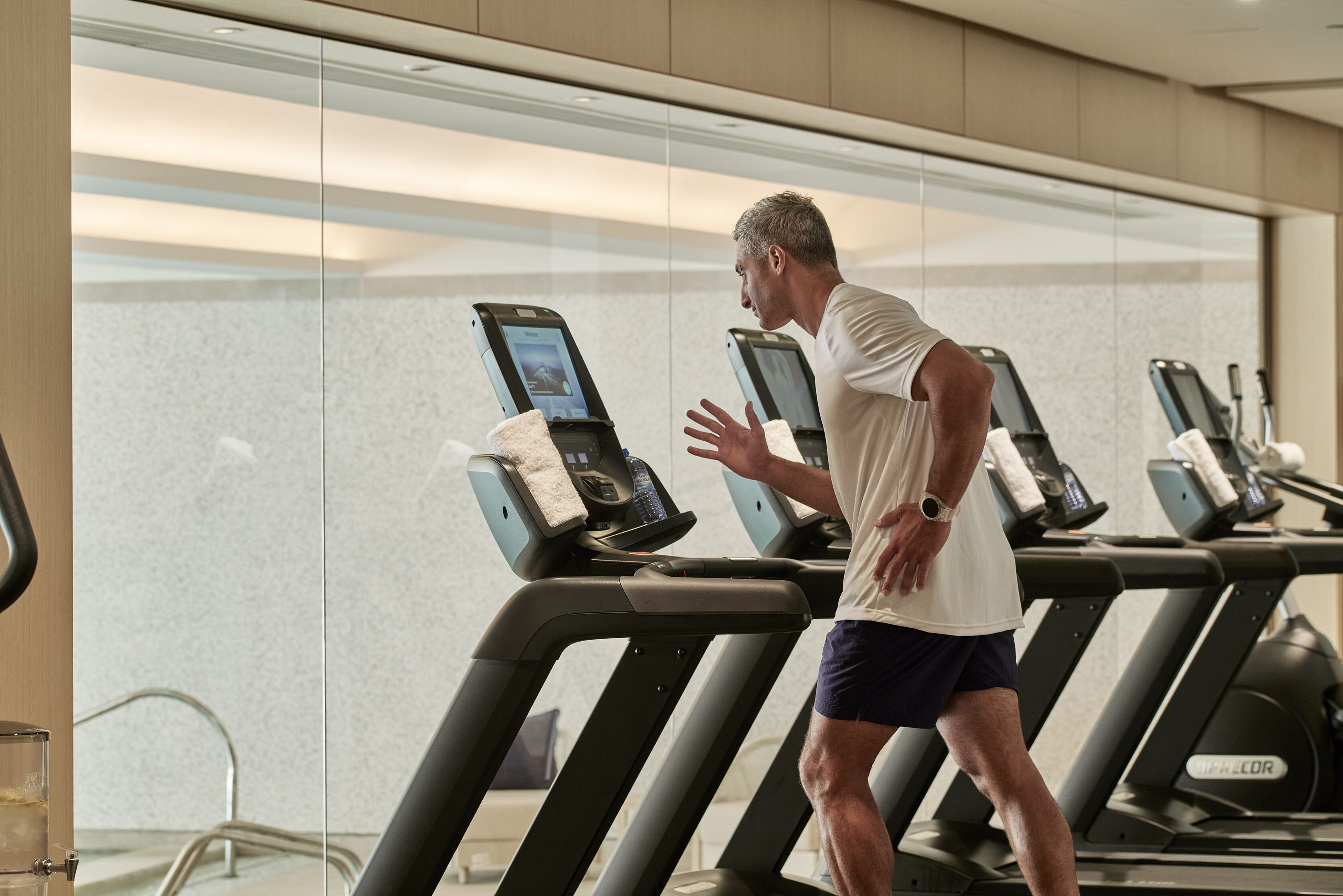 A man running on a treadmill in a gym with mirrored walls and multiple treadmills.