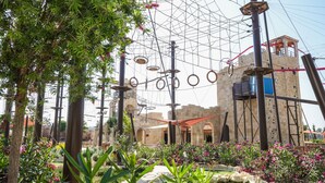 An outdoor obstacle course with climbing walls and rings, surrounded by greenery and flowers. - City of Dreams Mediterranean - Integrated Resort, Casino & Entertainment (Limassol)