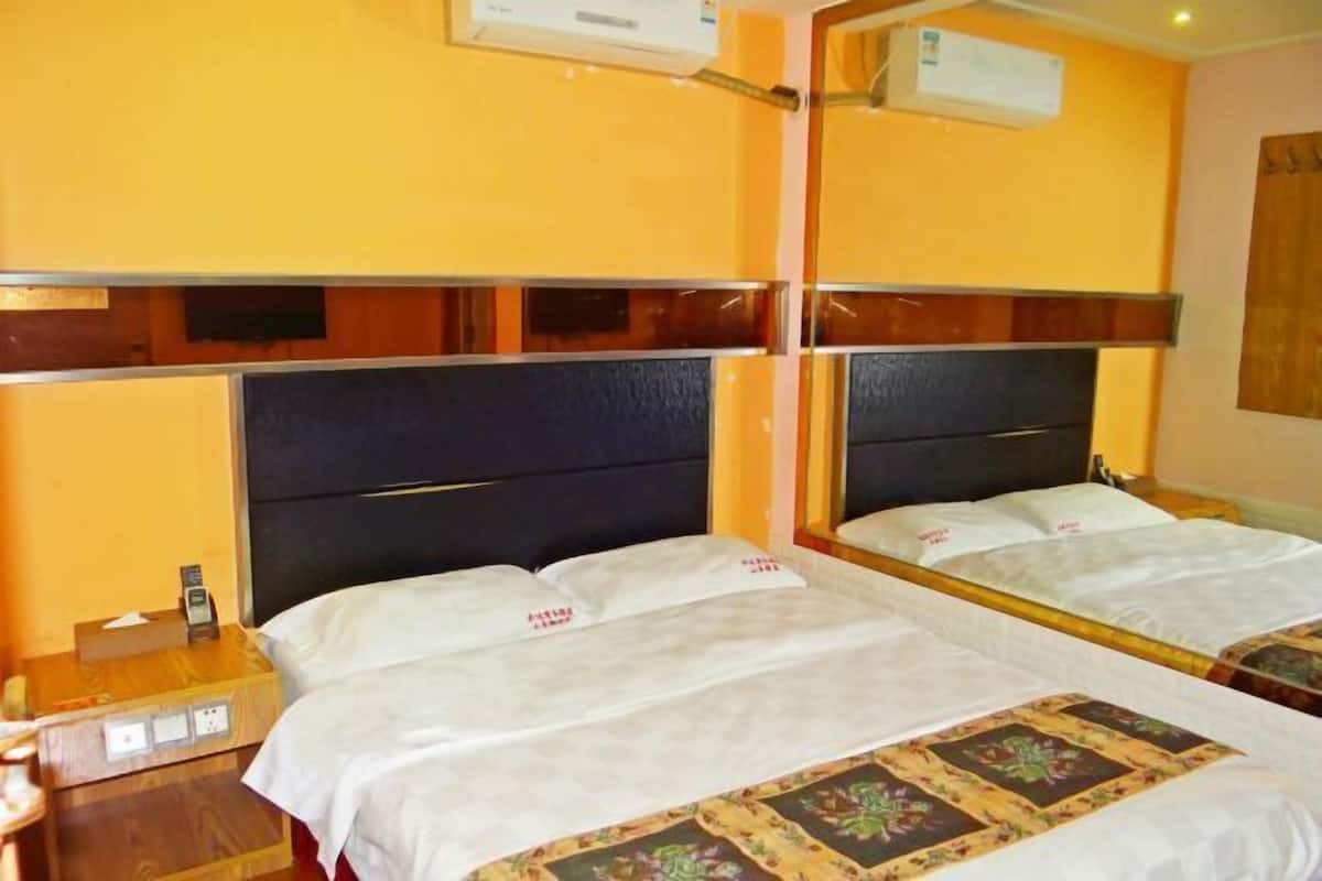 A hotel room with two beds, a wooden nightstand, an air conditioning unit, and a mirror.